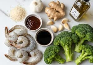 Shrimp and broccoli bowl ingredients arranged on marble counter including shrimp, broccoli, sauces, and rice