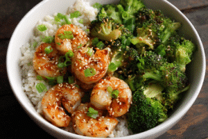Shrimp and broccoli bowl with jasmine rice, sesame seeds, and scallions on wooden table
