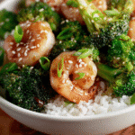 Shrimp and broccoli bowl with jasmine rice, sesame seeds, and scallions on wooden table
